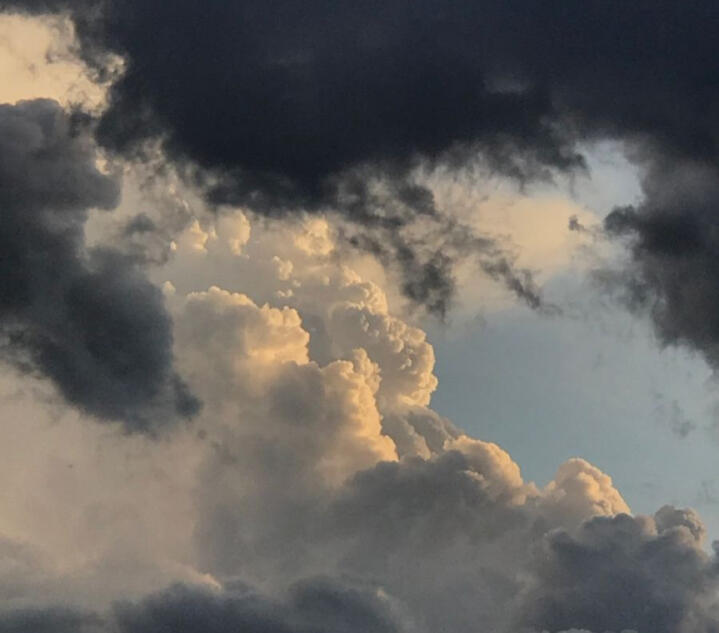 Two large clouds in the sky. The cloud closer to the camera is very dark and surrounds the top edge of the photo.