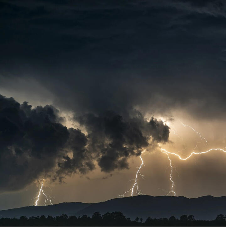 A very dark storm cloud with yellow lightning coming out of the bottom. There are 4 lightning strikes coming out.